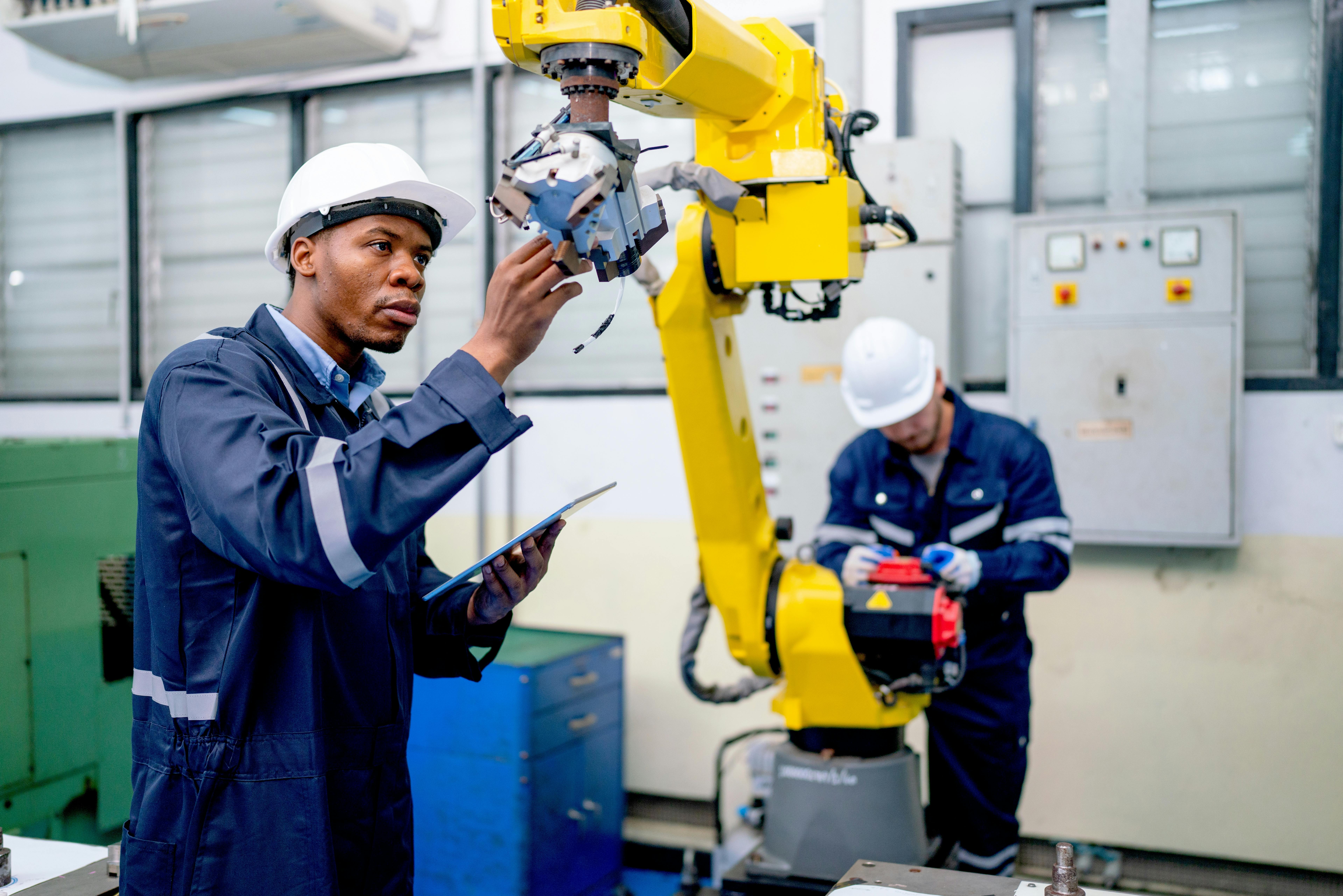engineer or technician worker hold part of robotic arm and check the function of machine and co-worker support in the back in factory workplace