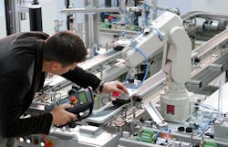 Man is holding teach panel to control a robotic arm, which is integrated on smart factory production line Man is holding teach panel to control a robotic arm, which is integrated on smart factory production line
