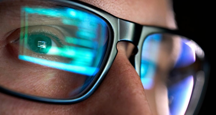 Focused developer coder wears glasses working on computer looking at programming code