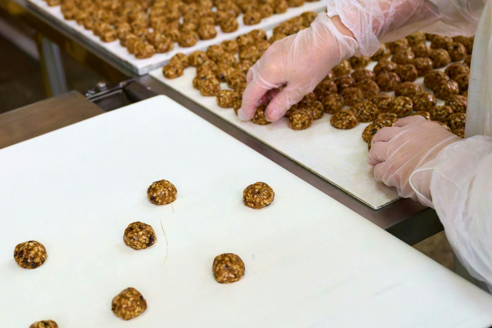 Workers carefully place grillage on a conveyor in a food production facility during busy daytime operations, ensuring quality and consistency of the product.