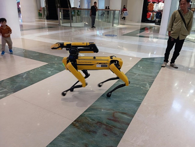 A yellow multipurpose robot dog or robodog by Boston Dynamics being exhibit at a shopping center