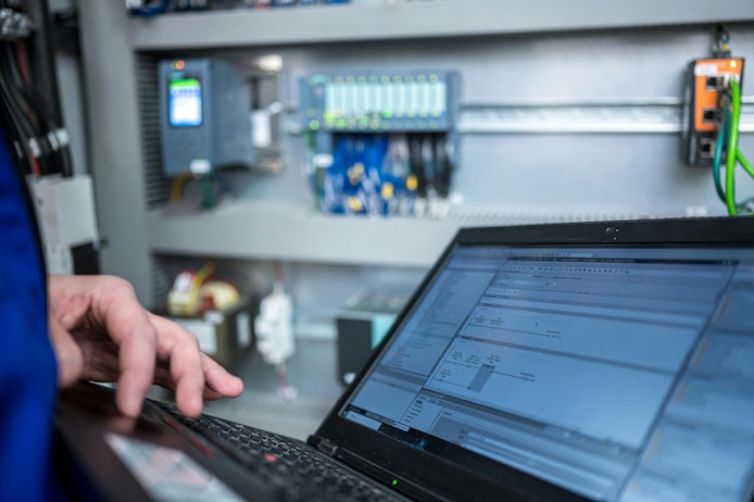 Programmer of PLC checks correct function of program in PLC with electrical cabinet in background