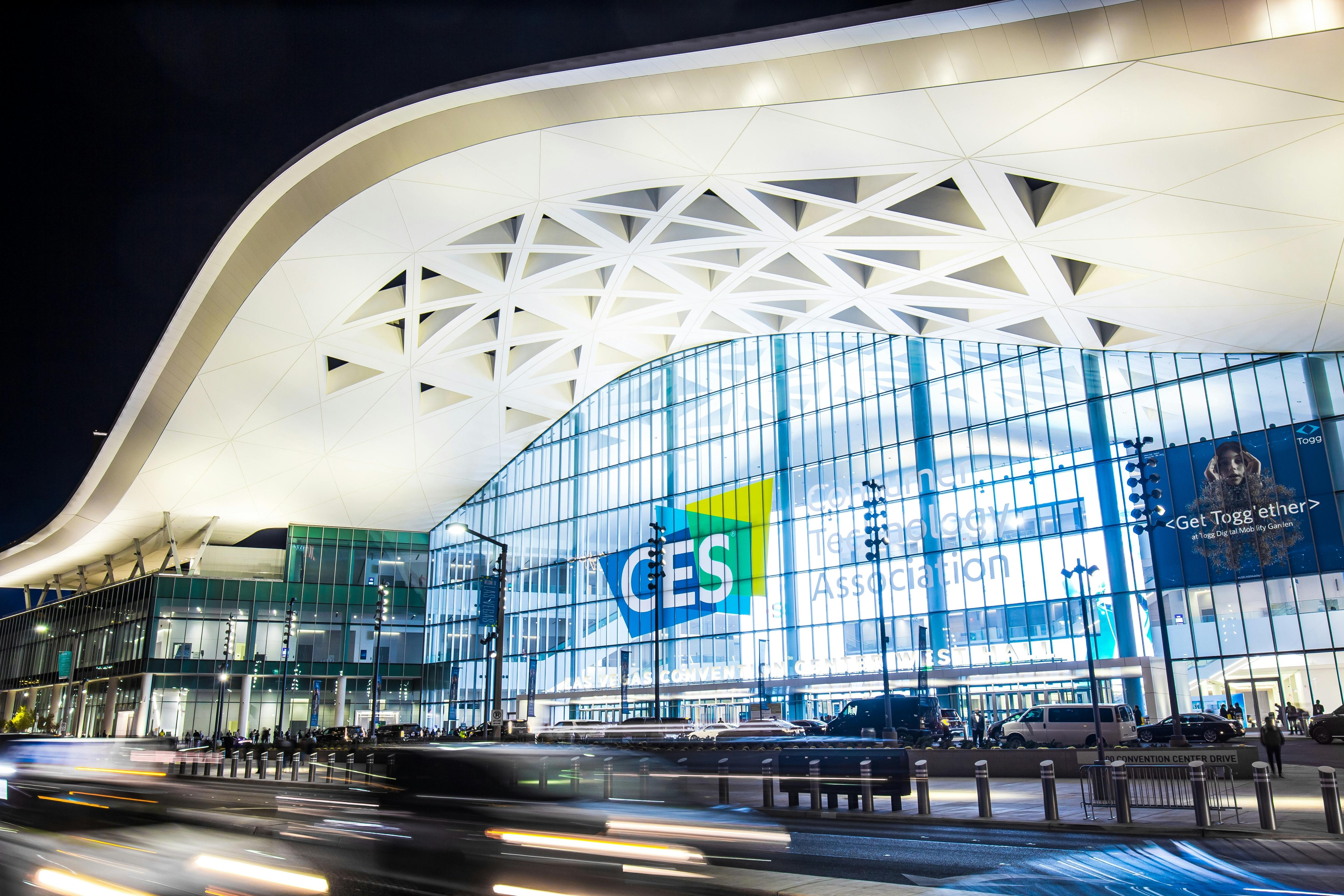 Exterior of Convention Center West Hall during CES2023. Logo of CES on glass wall. Light trails from car headlights of traffic passing by. Captured in long exposure.