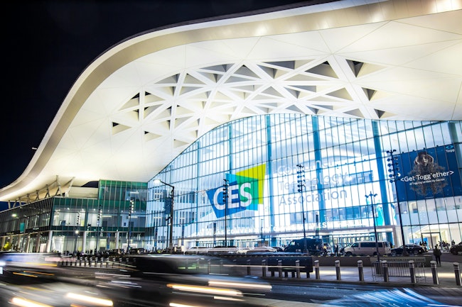 Exterior of Convention Center West Hall during CES2023. Logo of CES on glass wall. Light trails from car headlights of traffic passing by. Captured in long exposure.