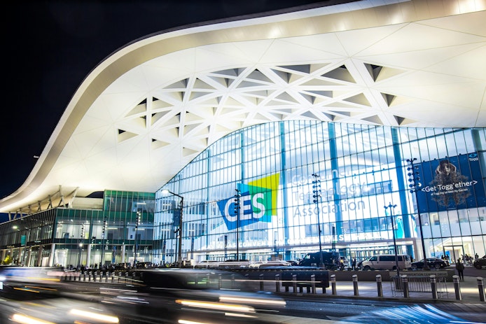 Exterior of Convention Center West Hall during CES2023. Logo of CES on glass wall. Light trails from car headlights of traffic passing by. Captured in long exposure.