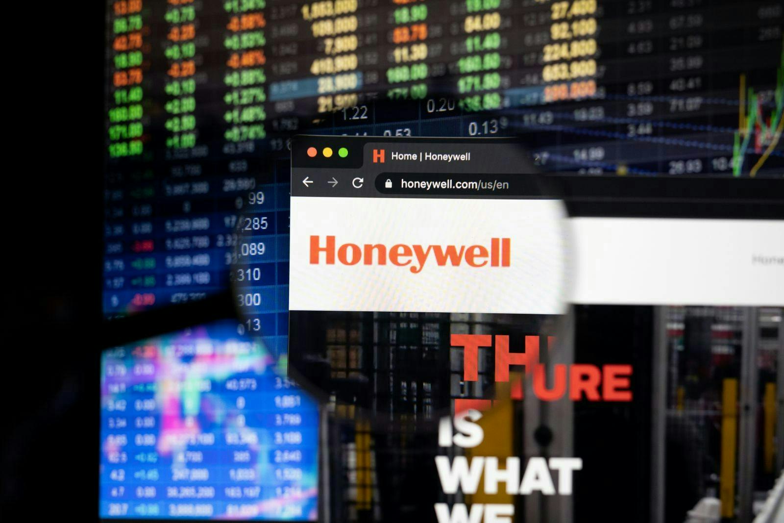 Honeywell company logo on a website with blurry stock market developments in the background, seen on a computer screen through a magnifying glass.