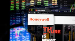 Honeywell company logo on a website with blurry stock market developments in the background, seen on a computer screen through a magnifying glass.