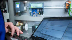 Programmer of PLC checks correct function of program in PLC with electrical cabinet in background