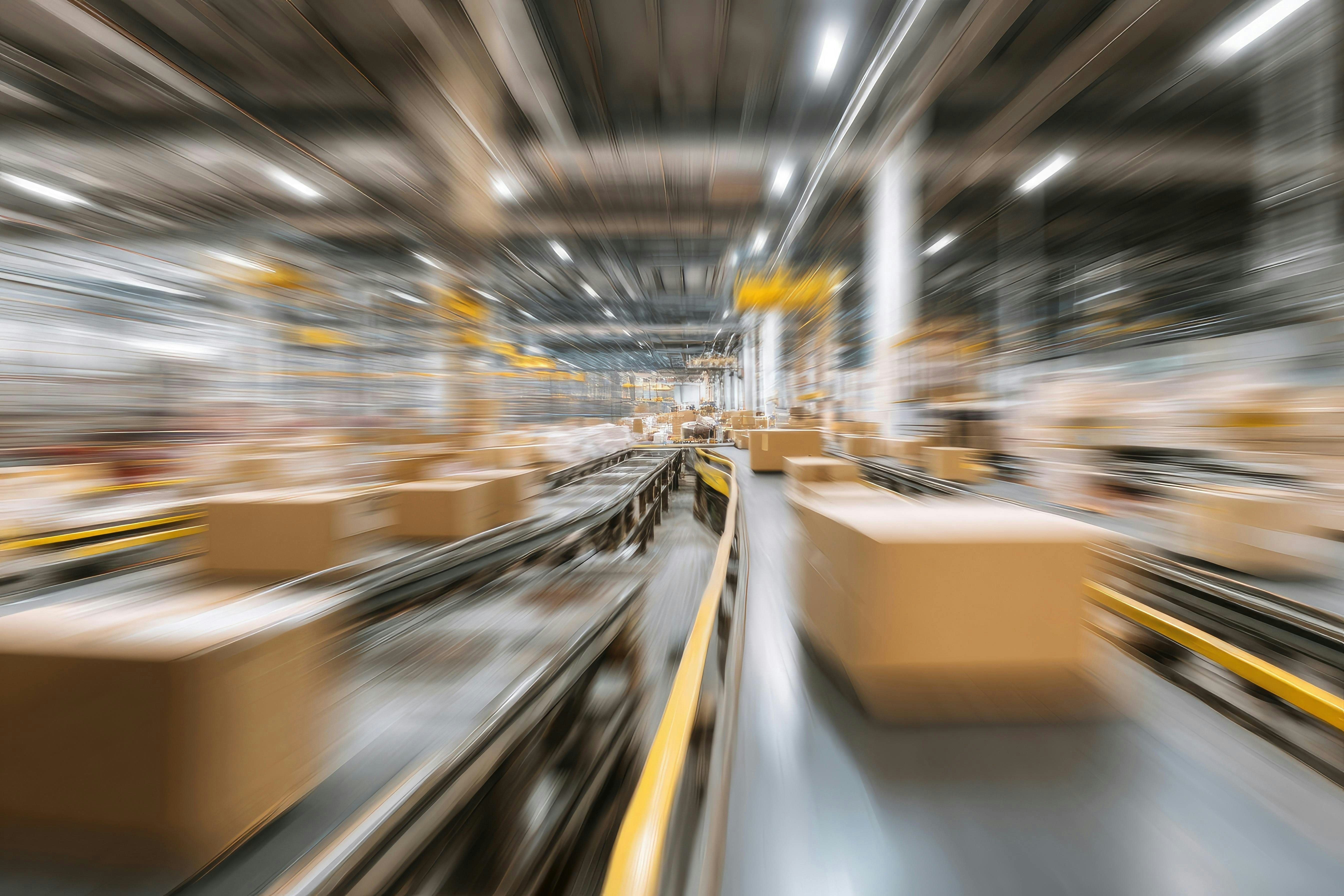 Fast-moving cardboard boxes on conveyor belts in a large warehouse or distribution center.