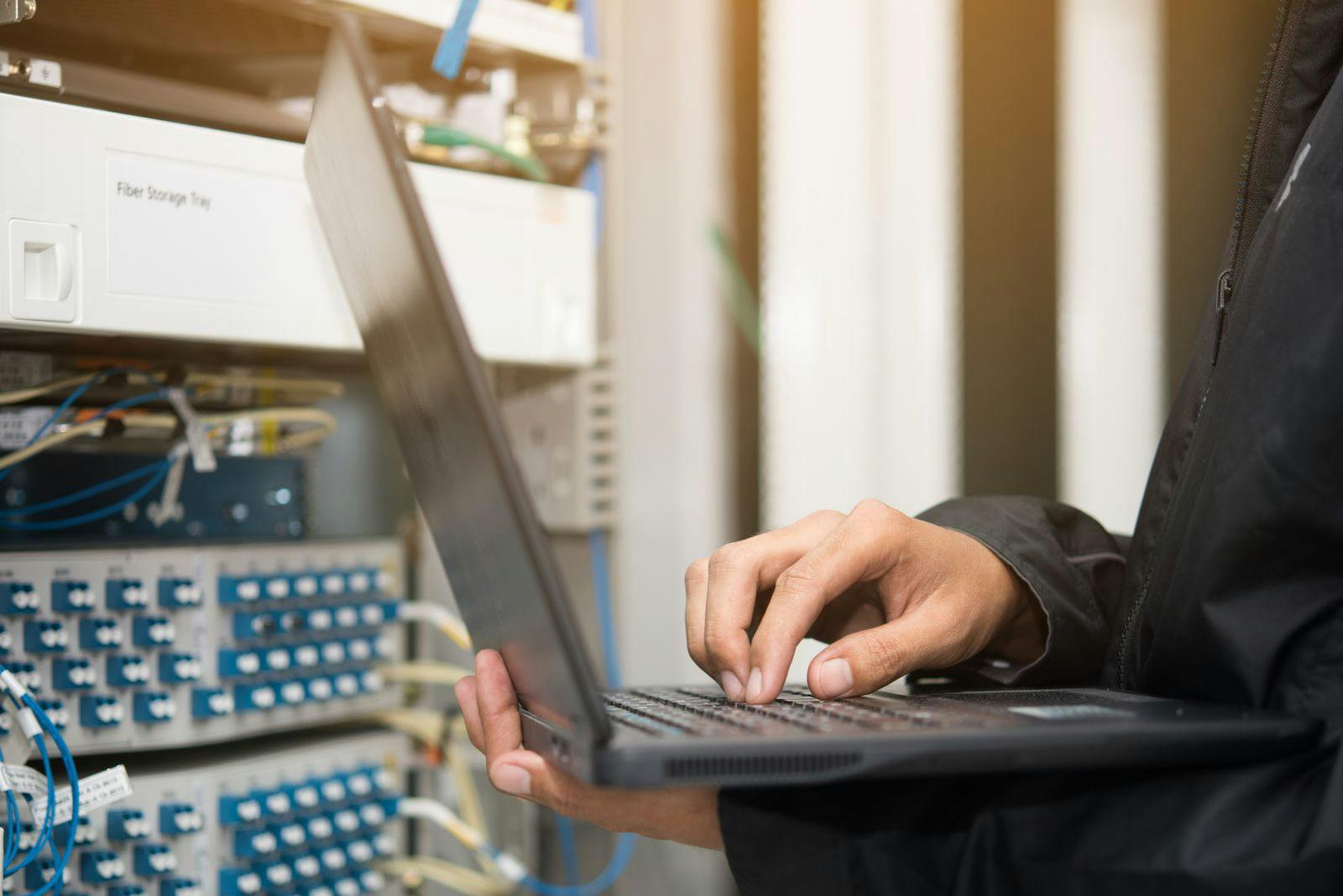 Technician using laptop in server room.