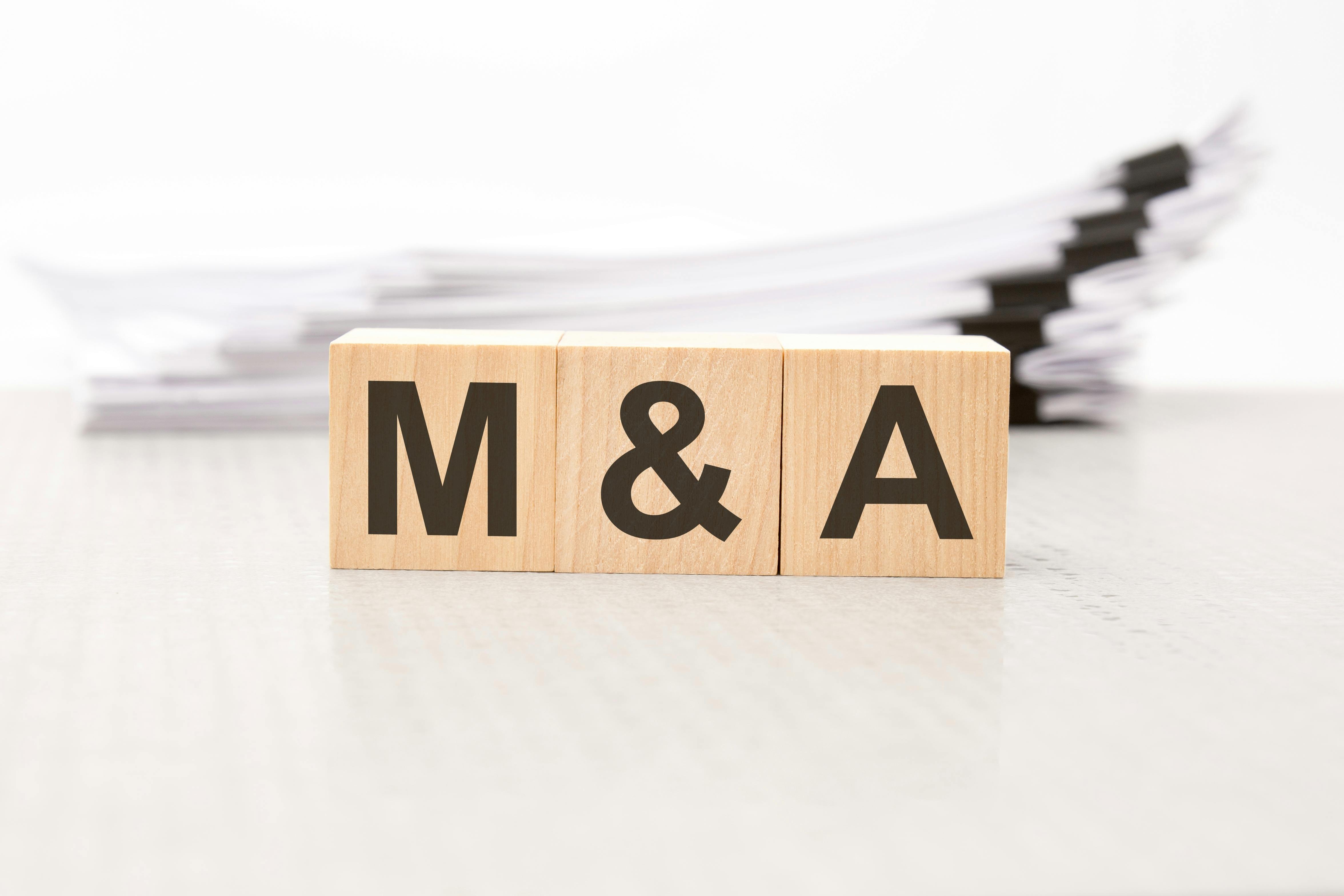 text m and a - Mergers and Acquisitions - on wooden blocks. the background is a business papers. finance concept. white background