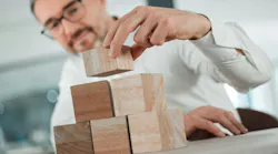 Start building your future from now. Shot of an unrecognisable businessman sitting alone in his office and using building blocks to plan.