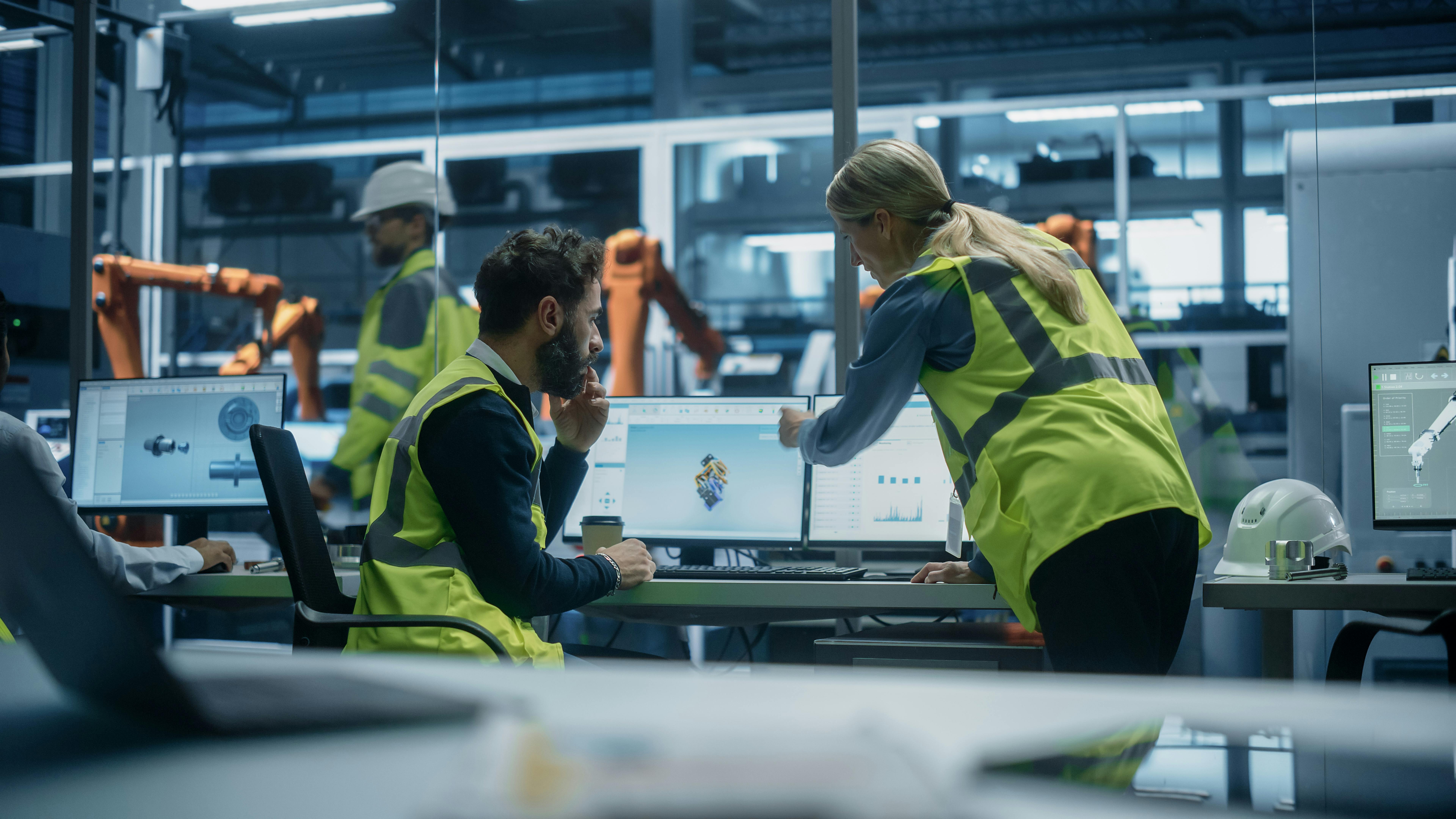 Male Industrial Engineer Showing Machine Component 3D Render To Female Manager On Desktop Computer. Automated Robot Arm Assembly Line Manufacturing Machinery.