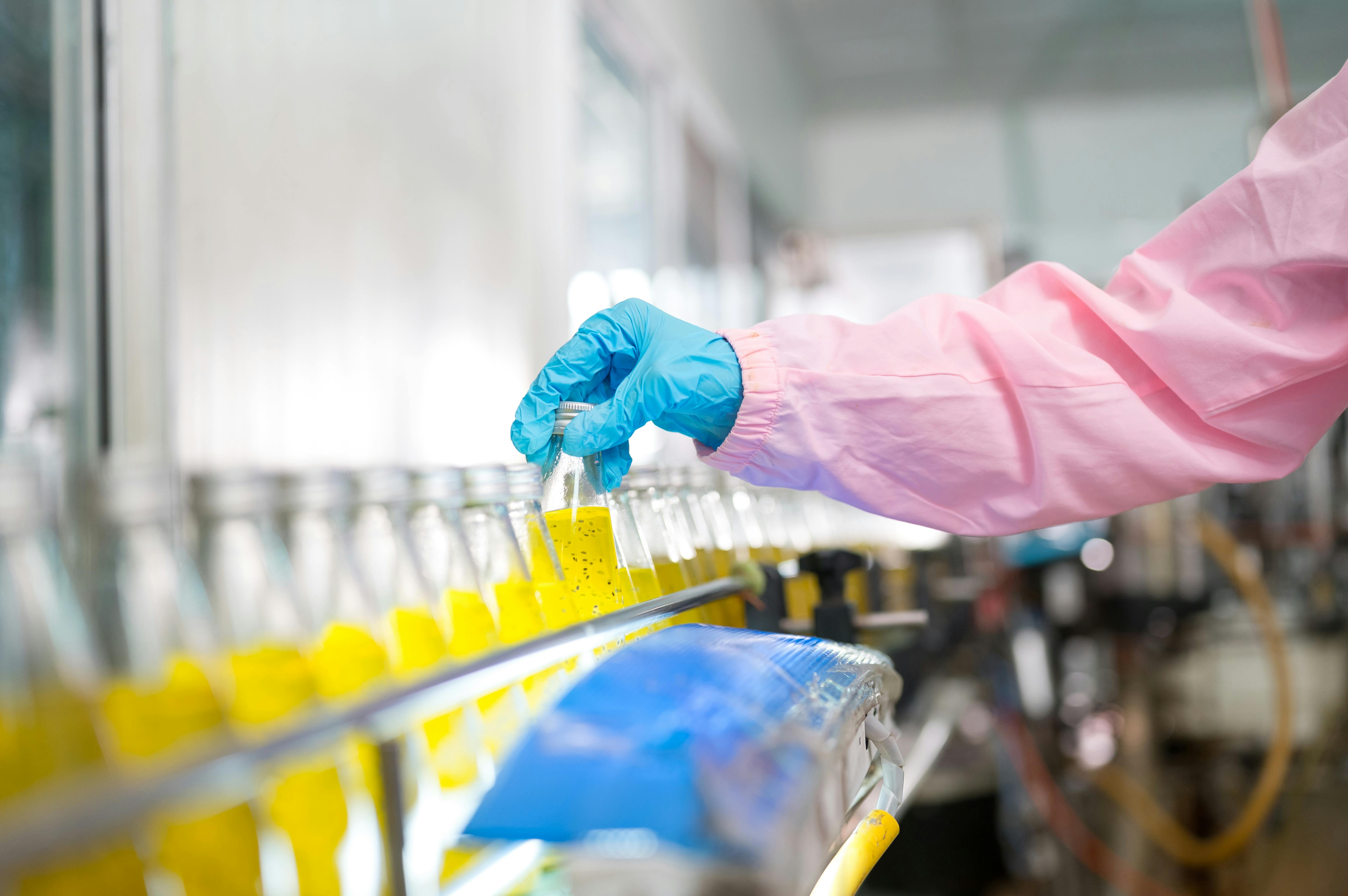 Female quality control inspector checking bottled fruit juice on production line in beverage factory, using tablet for monitoring and inspection