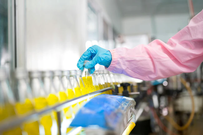 Female quality control inspector checking bottled fruit juice on production line in beverage factory, using tablet for monitoring and inspection
