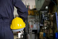 Back view close up of mechanic or worker holding yellow hard hat and wearing blue bear suit in factory with factory background. Back view close up of mechanic or worker holding yellow hard hat and wearing blue bear suit in factory with factory background.