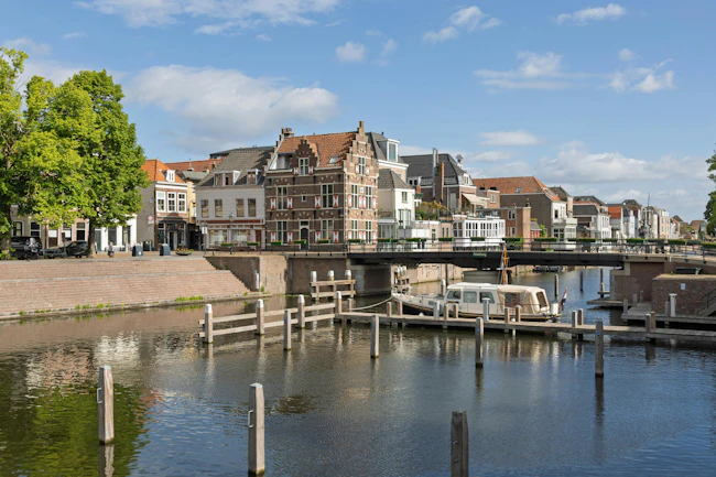 A picturesque scene in Gorinchem, Netherlands, showcasing traditional Dutch canal houses, the Peterbrug (Peter Bridge), and a house boat on the tranquil canal under a bright sky.