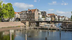 A picturesque scene in Gorinchem, Netherlands, showcasing traditional Dutch canal houses, the Peterbrug (Peter Bridge), and a house boat on the tranquil canal under a bright sky.