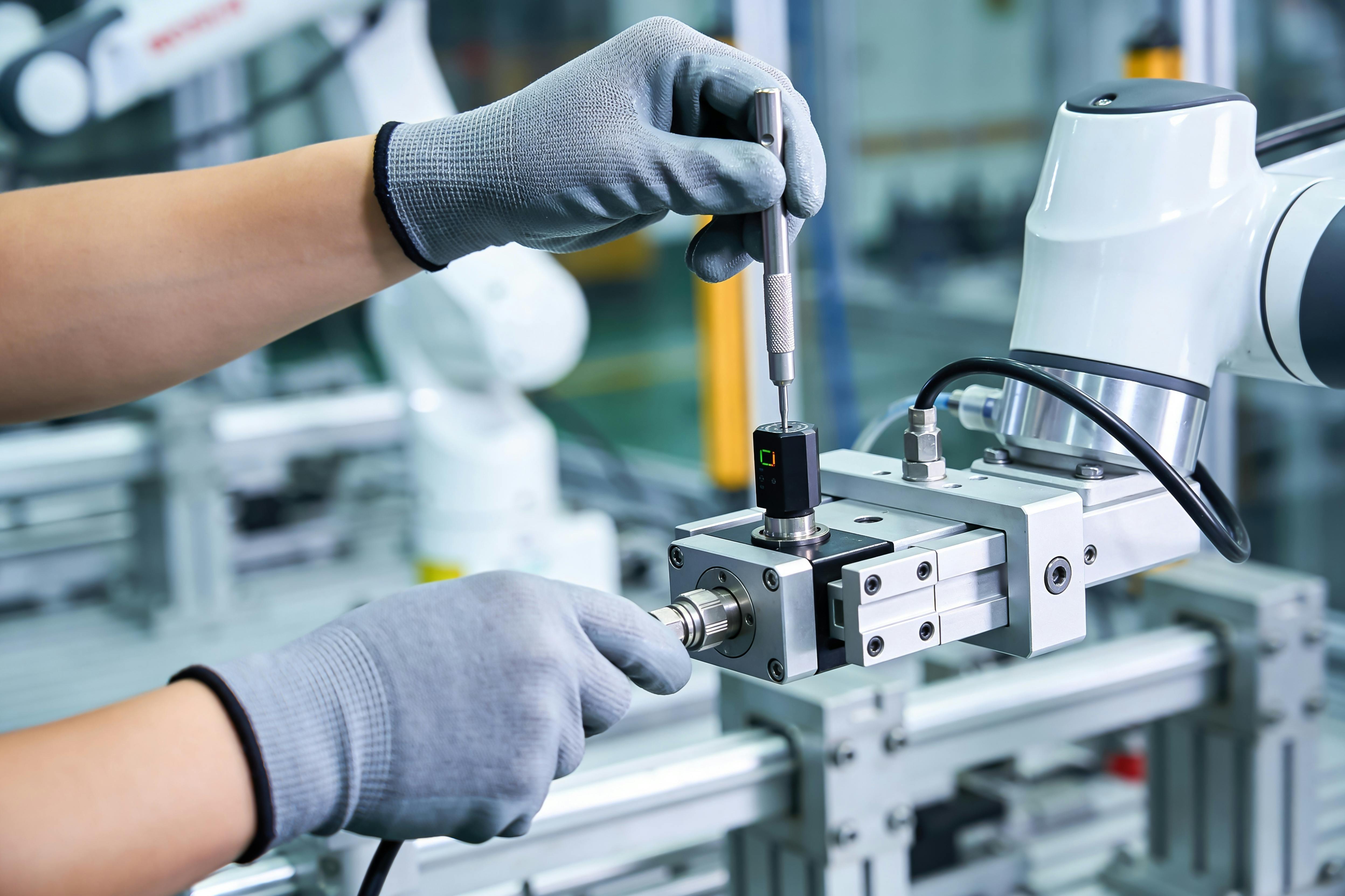 A worker in protective gloves carefully adjusts a sensor on an automated assembly line, highlighting advanced manufacturing processes and quality control