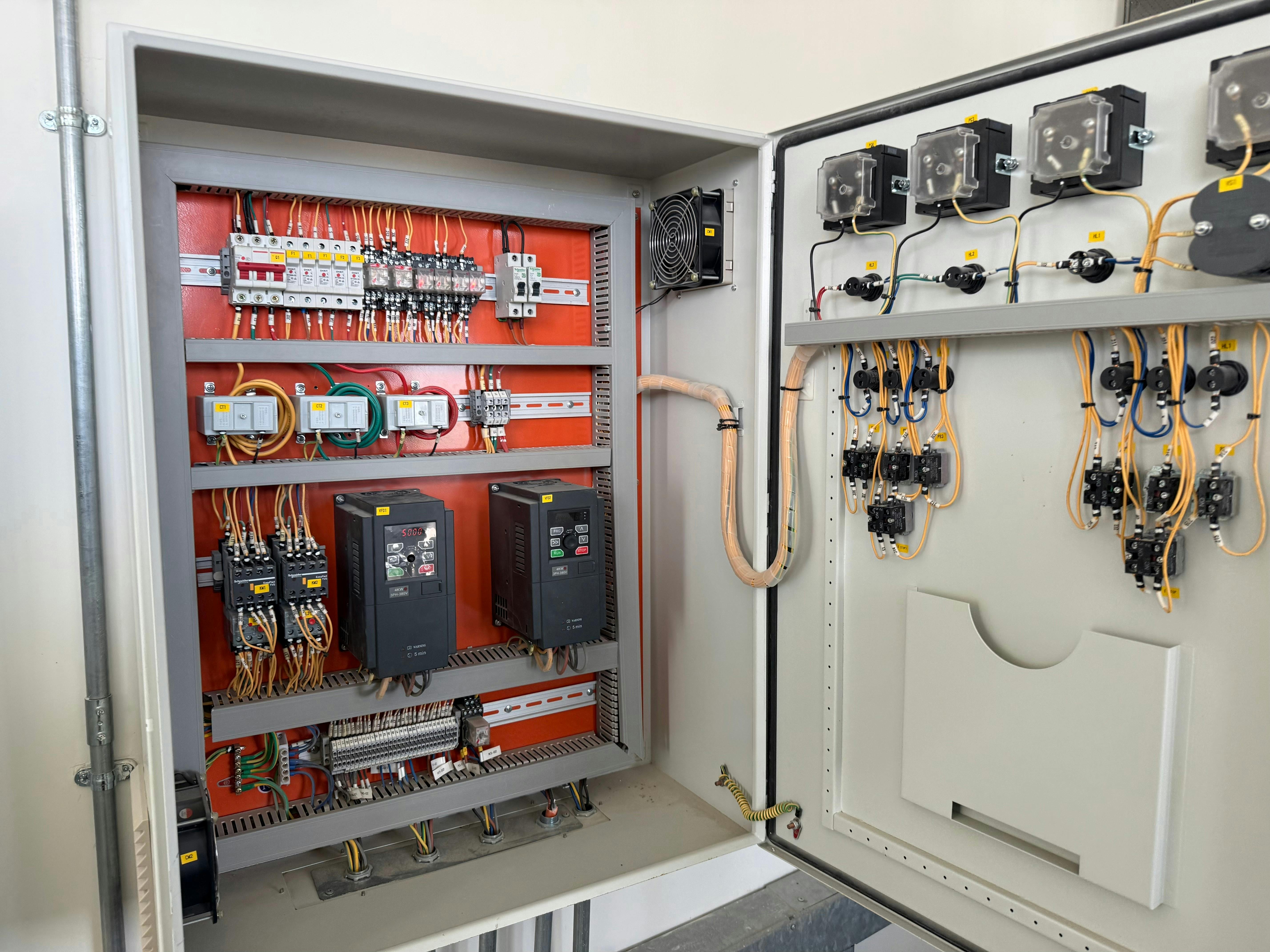 A meticulously organized industrial electrical control panel with its door open, revealing a complex network of wiring, circuit breakers, contactors, relays, and variable frequency drives (VFDs).