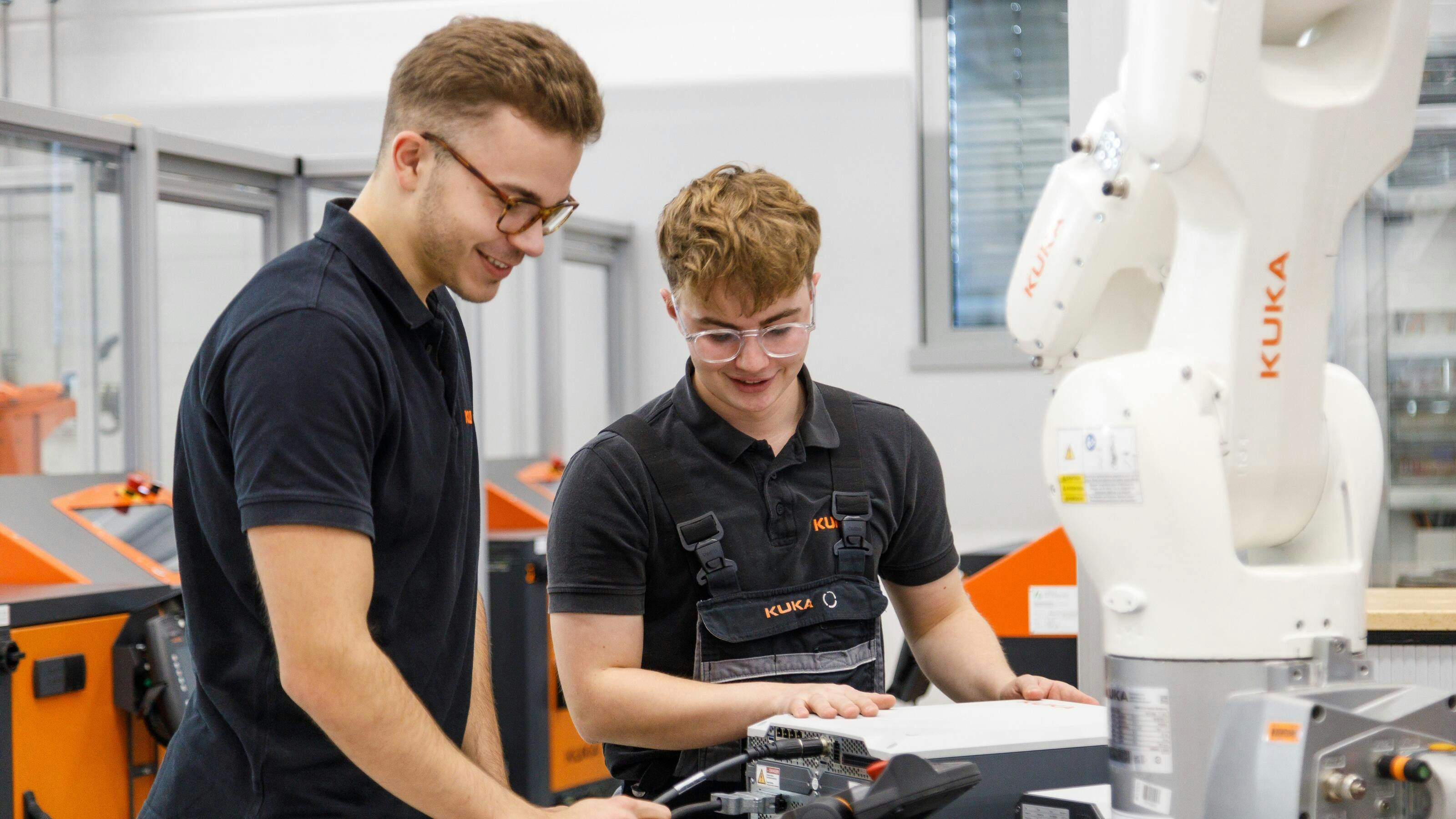 Two KUKA engineers examine robot programming in a robotics factory.