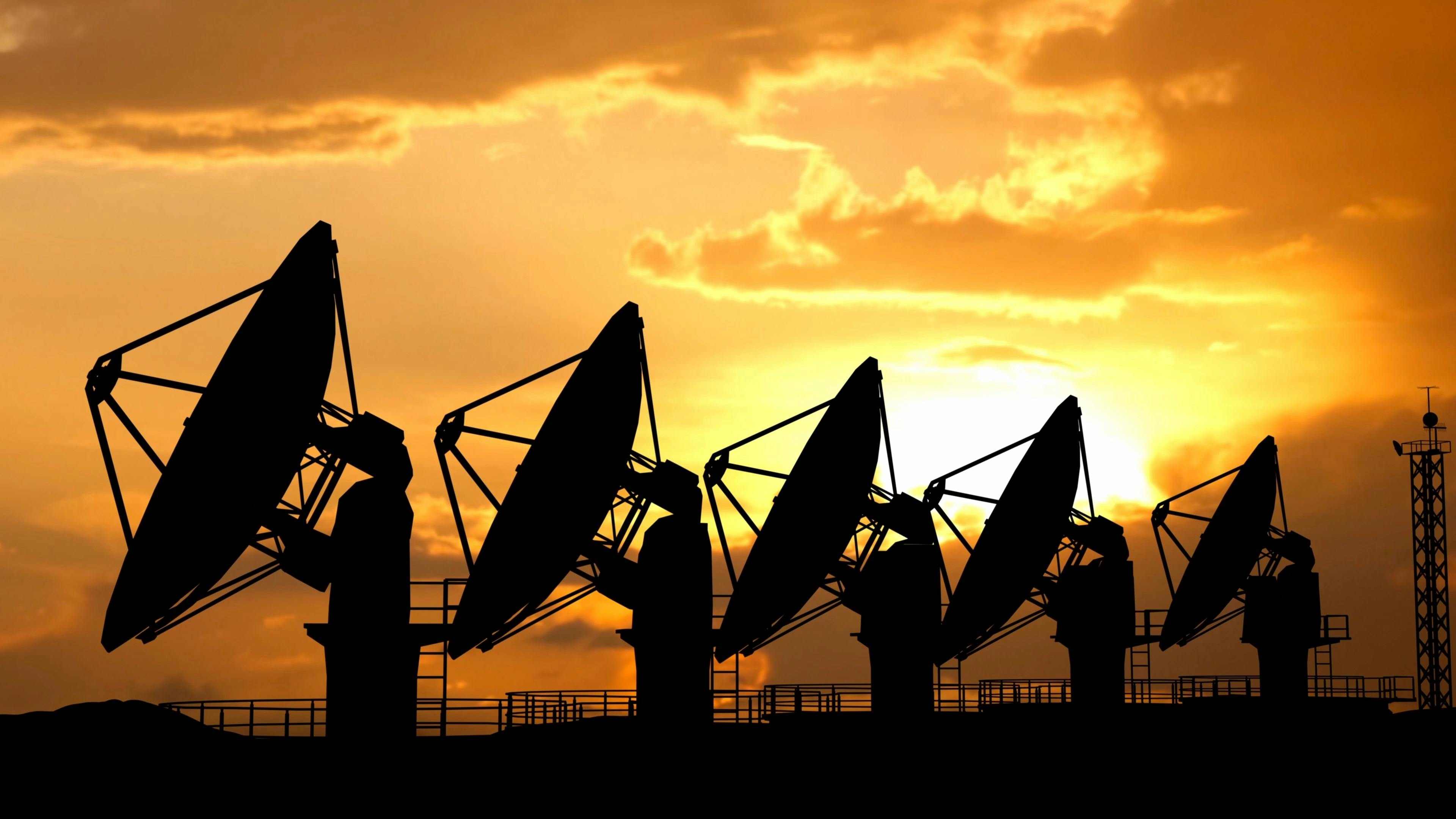Silhouettes of radars antennas on the ground against sunset sky. Row of large satellite stations dish telescopes.