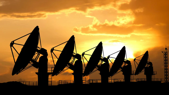 Silhouettes of radars antennas on the ground against sunset sky. Row of large satellite stations dish telescopes.
