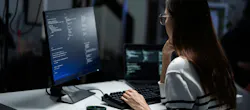 Rear view of a young programmer intensely reviewing code displayed on a monitor in a dark office.