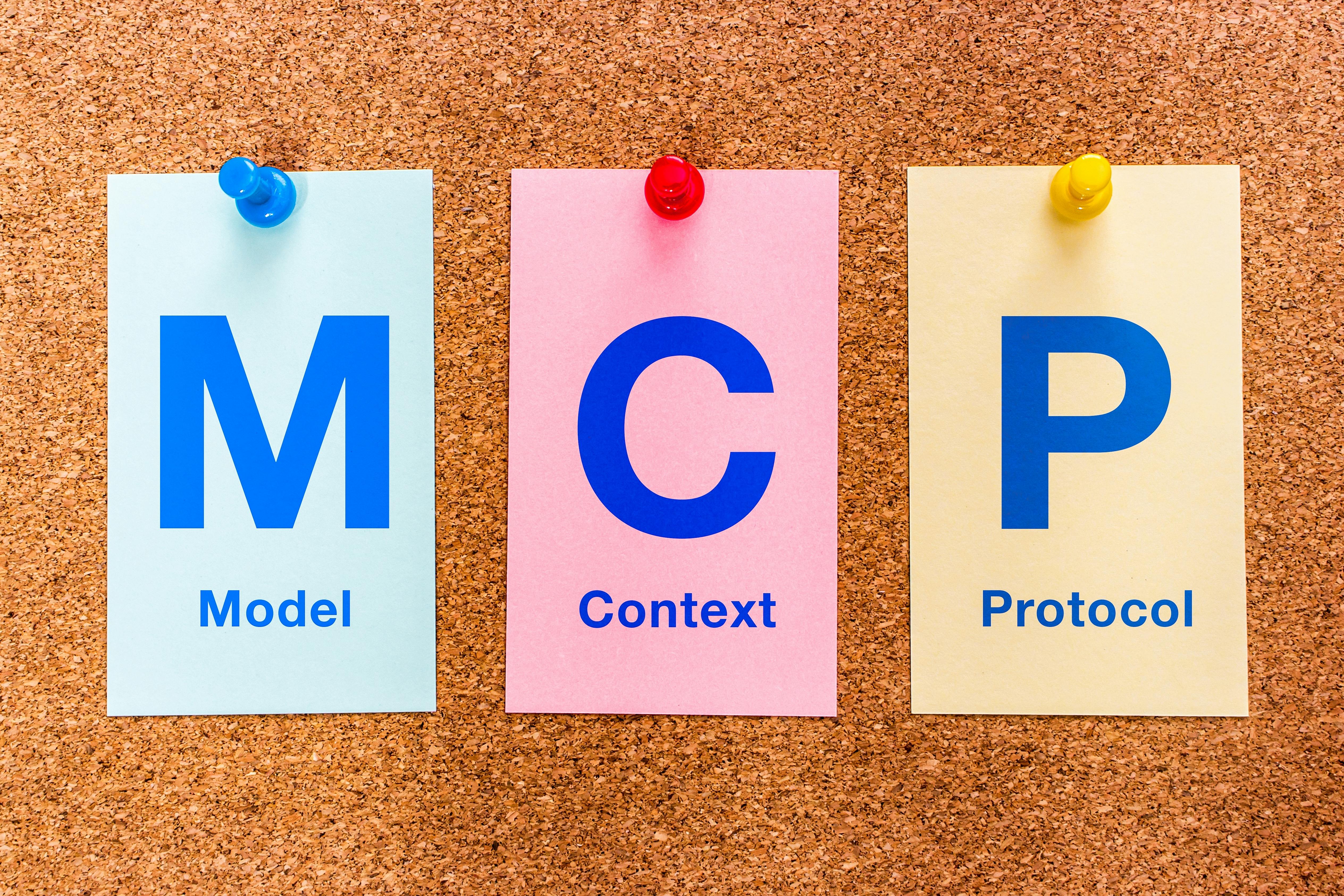 Three colored paper cards pinned to a cork bulletin board display the letters MCP (Model Context Protocol), illustrating the MCP standard for AI integration.