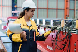 Female engineer carefully inspects roofing sheet production machine while holding blueprint at steel factory. Represents responsibility, accuracy, and industrial professionalism.