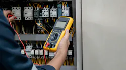 Engineer testing electrical system using a multimeter to measure the current at the control cabinet.