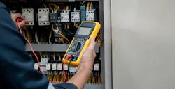 Engineer testing electrical system using a multimeter to measure the current at the control cabinet.