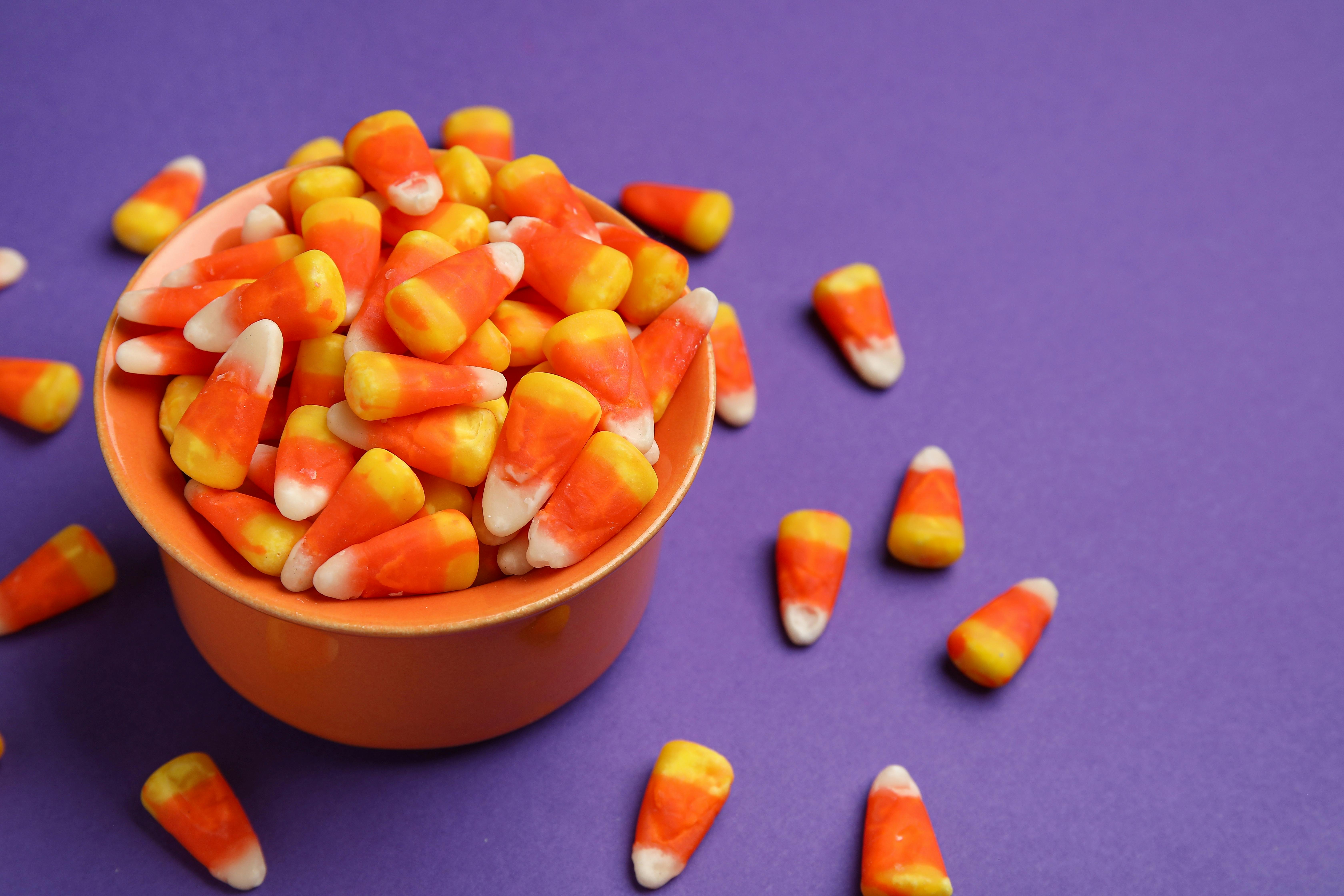 Bowl of tasty Halloween candy corns on purple background