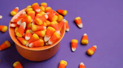Bowl of tasty Halloween candy corns on purple background