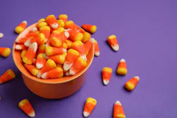 Bowl of tasty Halloween candy corns on purple background
