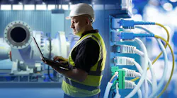 Industrial networking, equipment maintenance. Engineer uses laptop near network cables and machinery, monitoring systems and ensuring connectivity in production facility.
